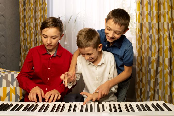 Three boys joyfully playing the piano together, sharing laughter.