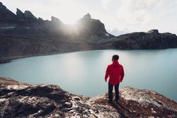 Back view of man in red jacket standing by lake waterside