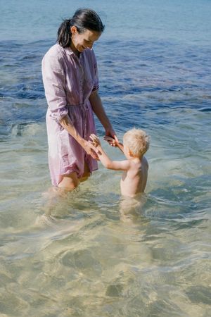 Woman and small kid having fun with water while relaxing on seacoast at resort