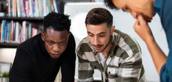 Multi-ethnic colleagues leaning over desk working on project