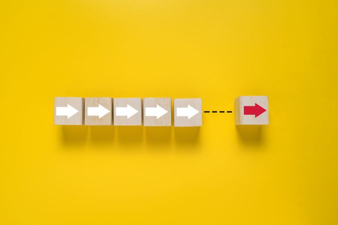 arrows and single red arrow pointing on wooden blocks isolated on yellow background. concept of leadership