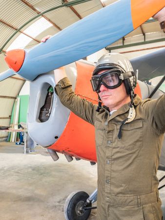 Confident pilot beside retro plane in hangar