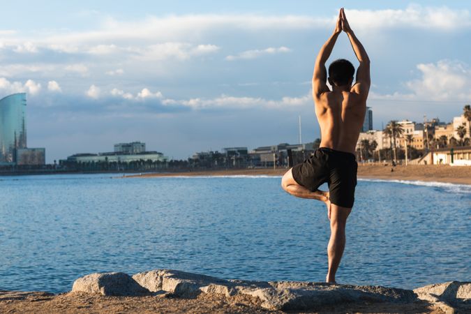 Shirtless man balancing in yoga pose on beach