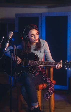Female singer playing guitar and performing a song in studio