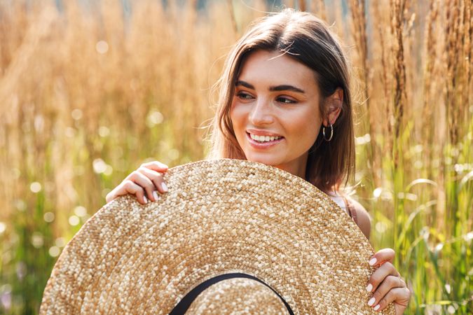 Woman standing in field outside holding up sunhat