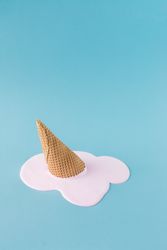 Melted pink ice cream and waffle cone on pastel blue background
