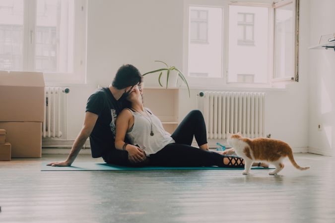 Loving couple cuddling on floor while cat walking around