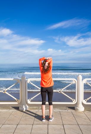 Athletic woman stretching triceps before running on the beach promenade on a summer morning, vertical
