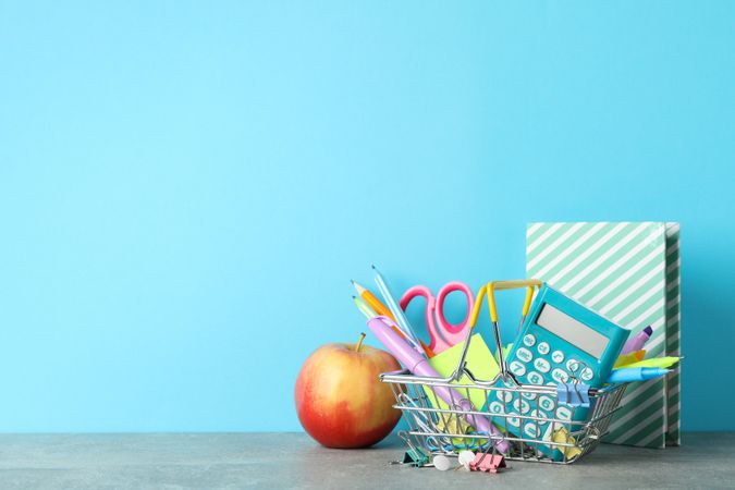 Basket of back to school supplies on desk with blue wall