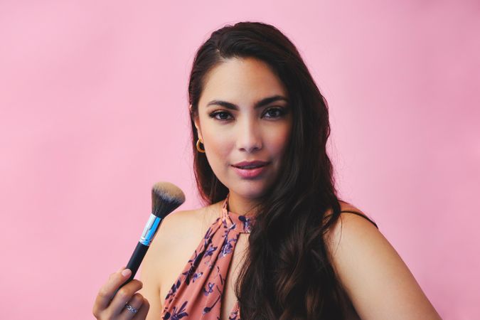 Head shot of serious Hispanic woman looking at camera while holding large make up brush
