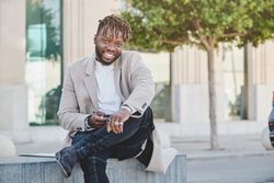 Cheerful Black man browsing cellphone while sitting on street
