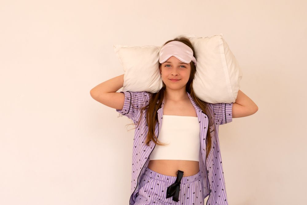 Relaxed girl with pillows, wearing sleep mask and pajamas.