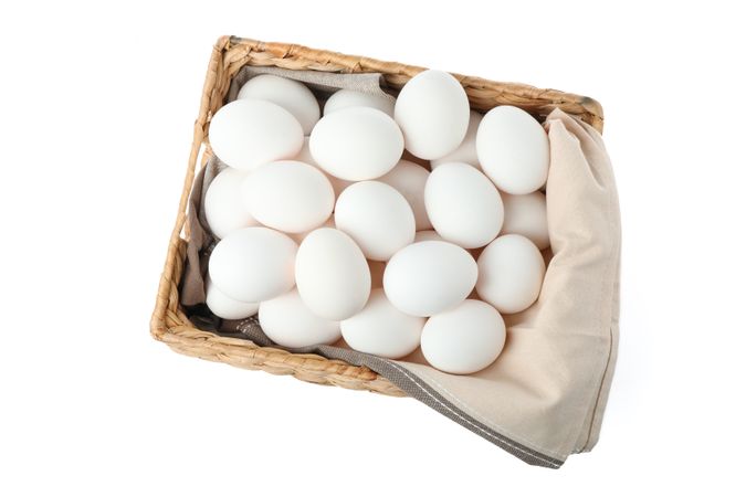 Chicken eggs with kitchen towel in straw basket isolated on plain background, top view