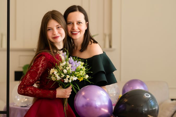 Teen girl holding bouquet flowers standing with woman.