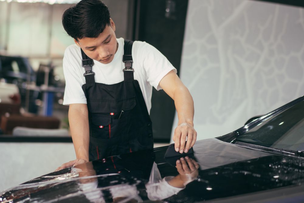 Asian man smoothing car wrap to front of vehicle