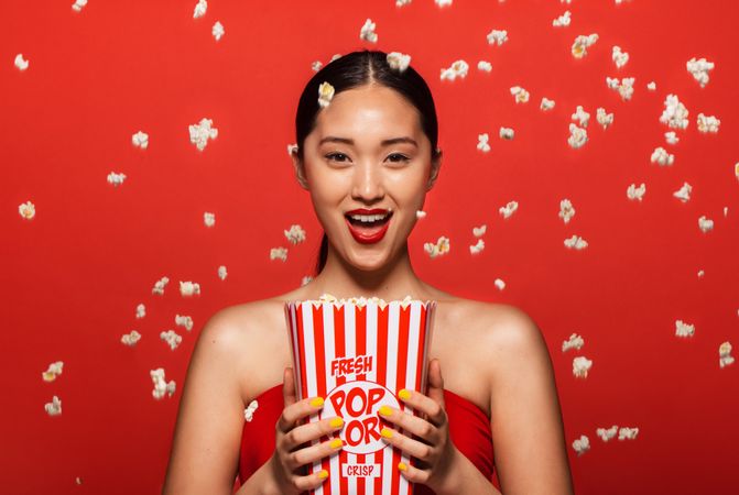 Young woman holding popcorn bucket with popcorn throw around her