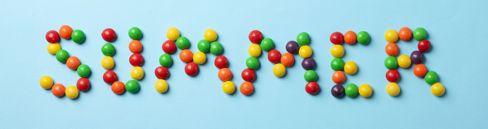 Word Summer made of candies on blue background, top view