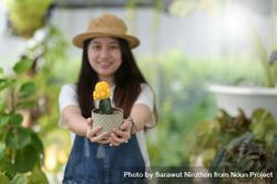 Asian female smiling and holding out a pot with a yellow cactus 43zEX5