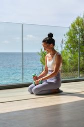 Sportswoman in activewear sitting in dumbbells on terrace against blue ocean