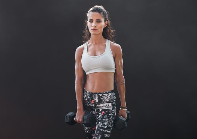 Woman exercising with dumbbells over dark background