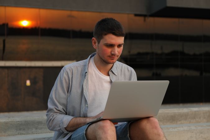 Young man sits in steps and working in laptop outdoor. Freelancer