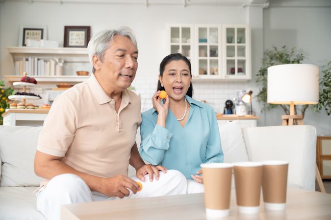 Asian couple playing toss ping pong ball to the cup at home