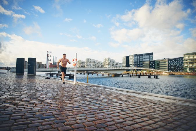 Athletic man running next to the river outside without a shirt
