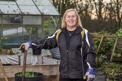 Older woman smiling outside greenhouse with shovel 41Knl0