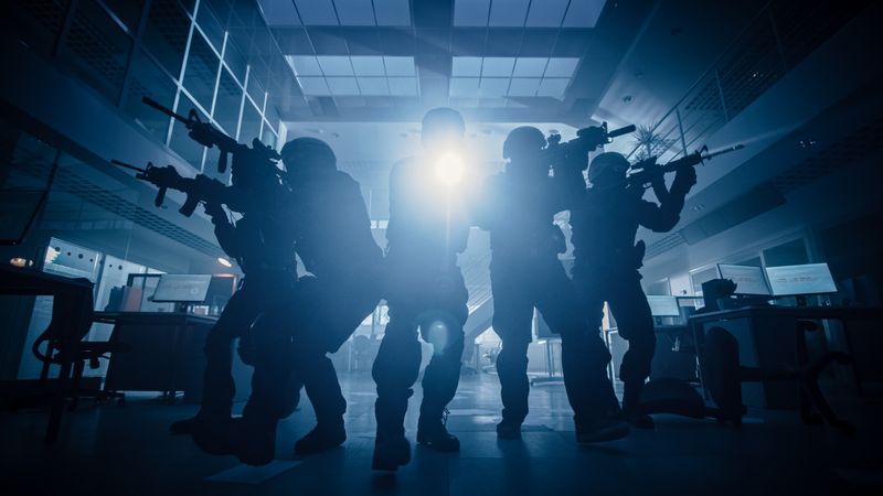 Masked Team of Armed SWAT Police Officers Move in a Hall of a Dark Seized Office Building with Desks and Computers.