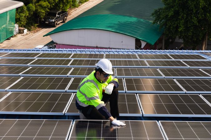 Male engineer checking solar cell  or photovoltaic cell by electronic device installed on the roof of the factory. Technician worker repair or inspect the system. Industrial renewable energy concept