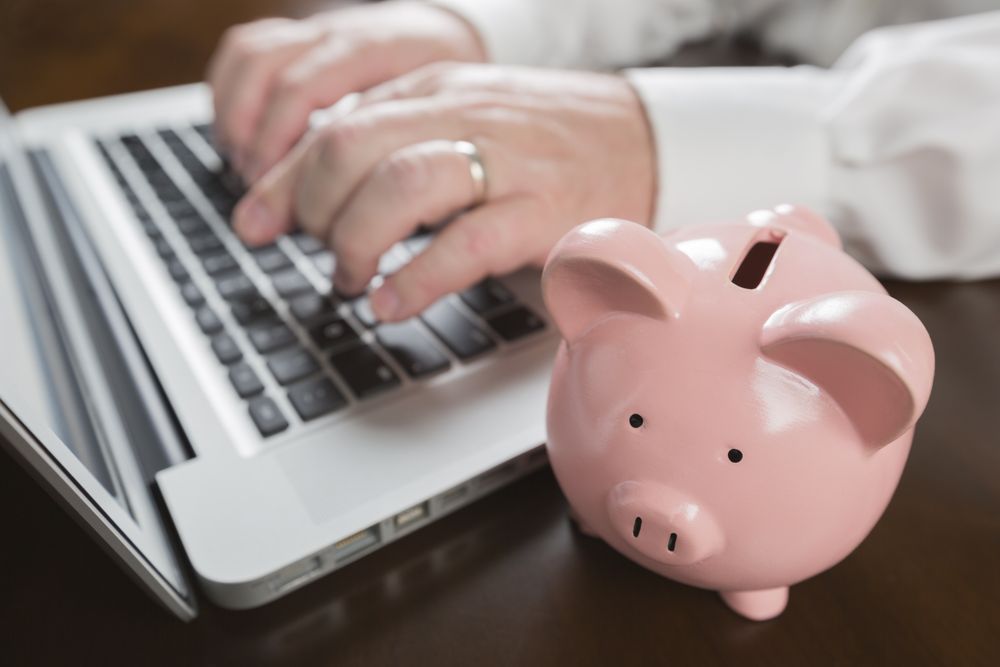 Piggy Bank Near Male Hands Typing on Laptop