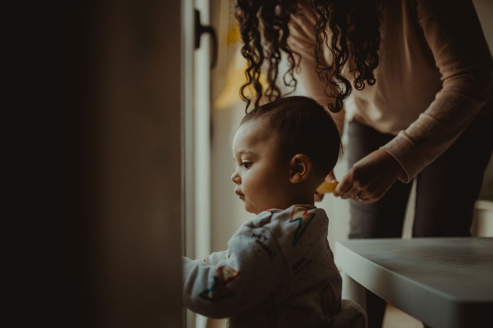 Toddler looking out the window with mother standing behind him