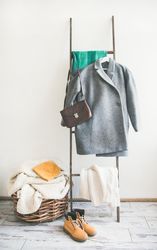 Woolen sweaters, grey scarf, winter boots on modern garment rack, with thatched basket, close up