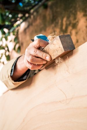 Anonymous mature man shaping wood with plane tool