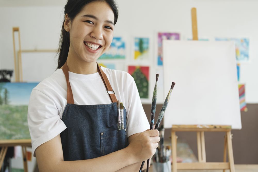Young Asian female artist in art studio look at camera and smiling.