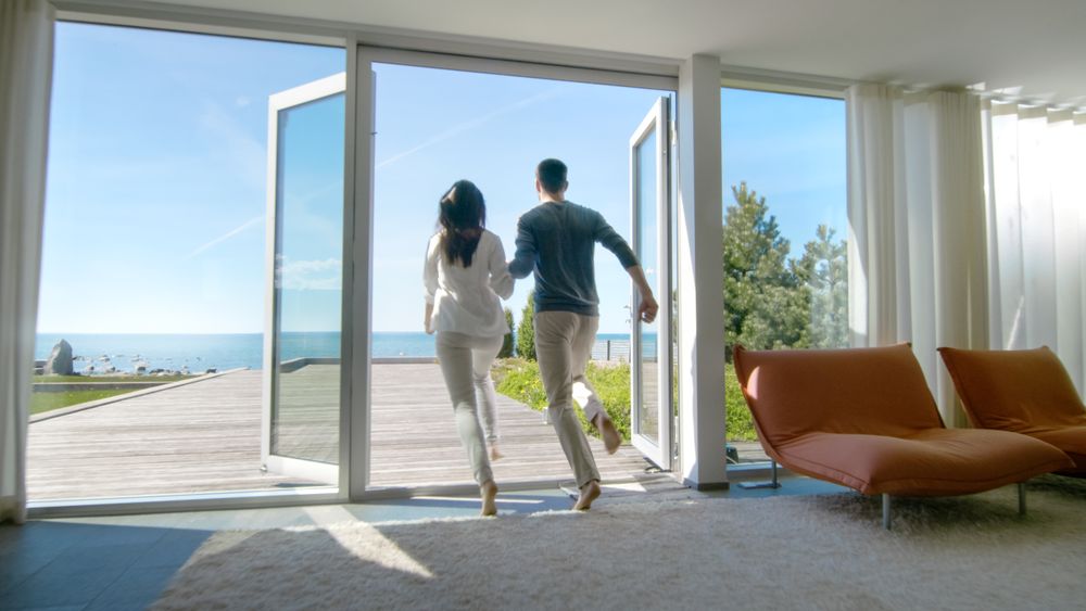 Happy Young Couple Holding Hands  Runs out of Their Home onto the Terrace with the Seaside View.