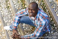 Happy male in plaid shirt sitting on stairs and looking up 4Axp85