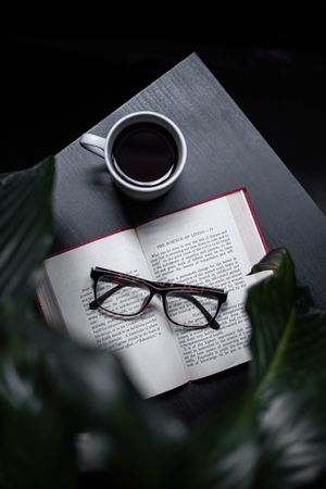 Framed eyeglasses on open book beside cup of coffee on a table