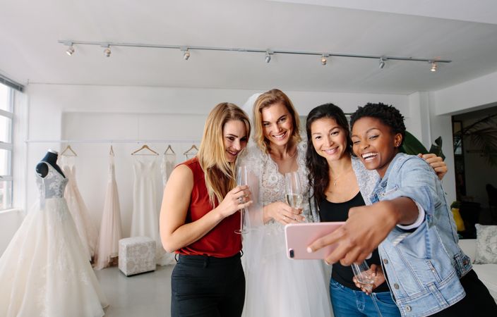 Woman in wedding gown with female friends taking selfie in bridal boutique