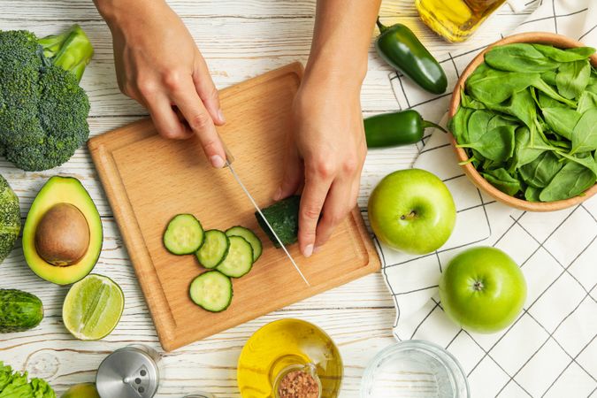Woman cutting cucumber on wooden table