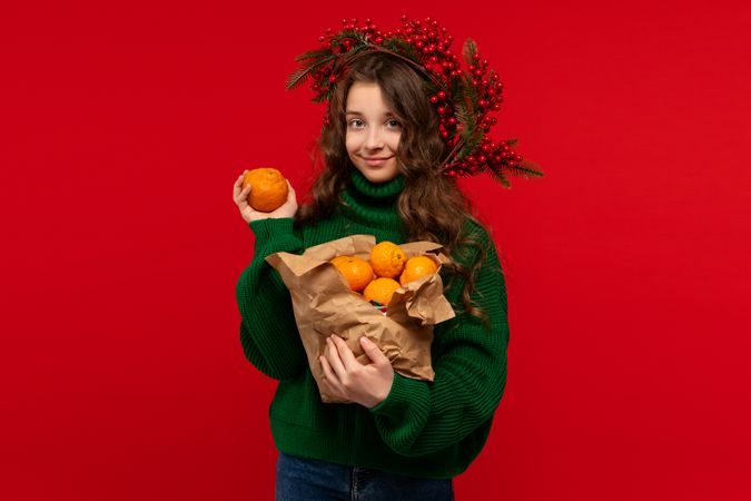 Young girl in green sweater holding oranges in paper bag