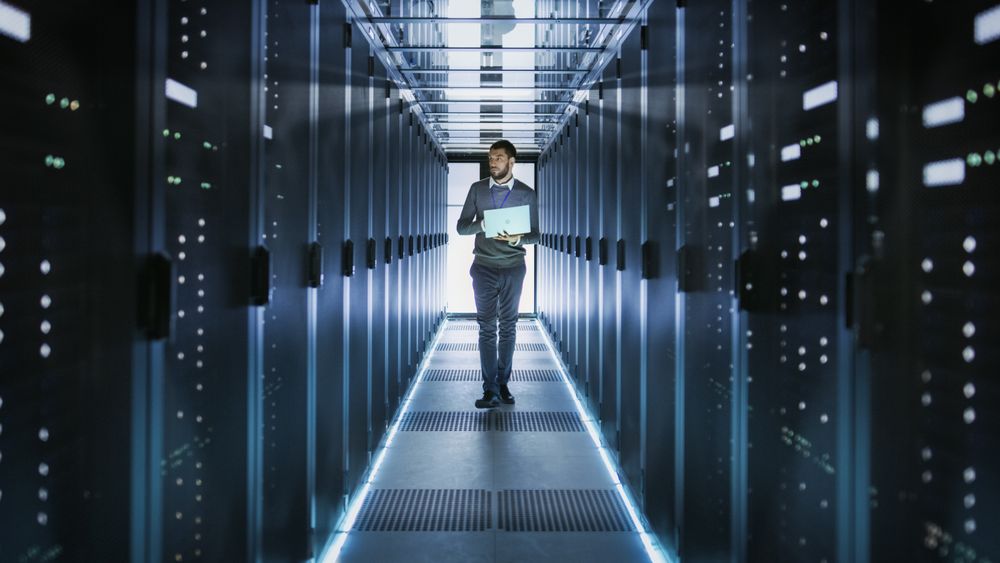 IT Technician Works on Laptop in Big Data Center full of Rack Servers.
