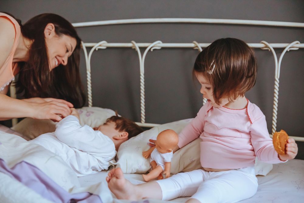 Closeup of happy little girl holding doll and cookie while mother plays with brother