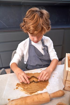 Boy cutting cookie dough on table