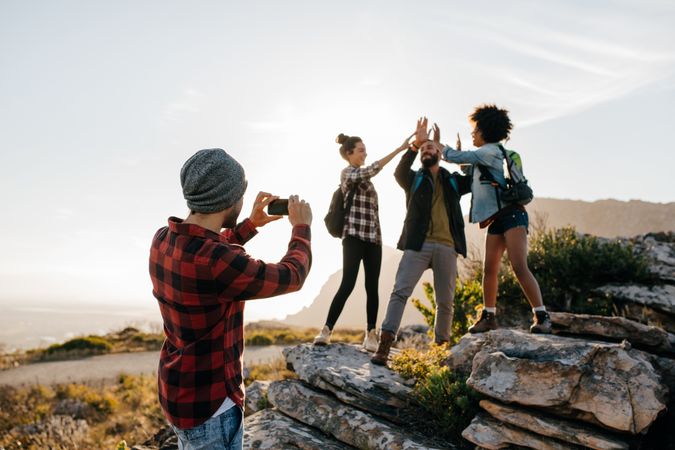 Young man taking pictures of his friends doing high five in countryside