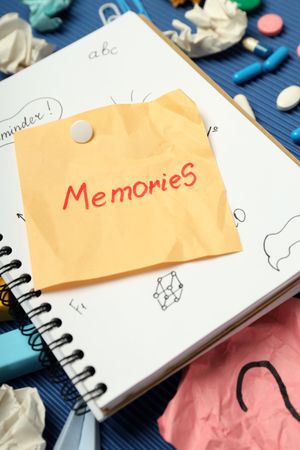 “Memories” post it note on book with pills, paper clips and pens, vertical closeup