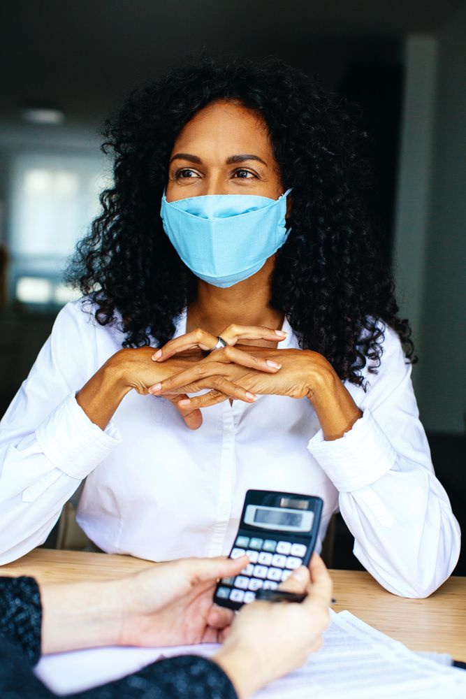 Woman working with a colleague with calculator wearing a facemask