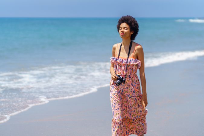 Female in maxi dress walking along coast with camera