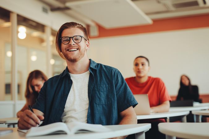 Young man in college classroom looking at camera and smiling
