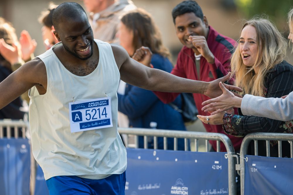 Marathon Audience Clapping and Cheering Their Loved Ones Participating in the Race: Black Athletic Male Marathon Runner Giving a High Five to Female Friend Supporting Him in the Audience While Running